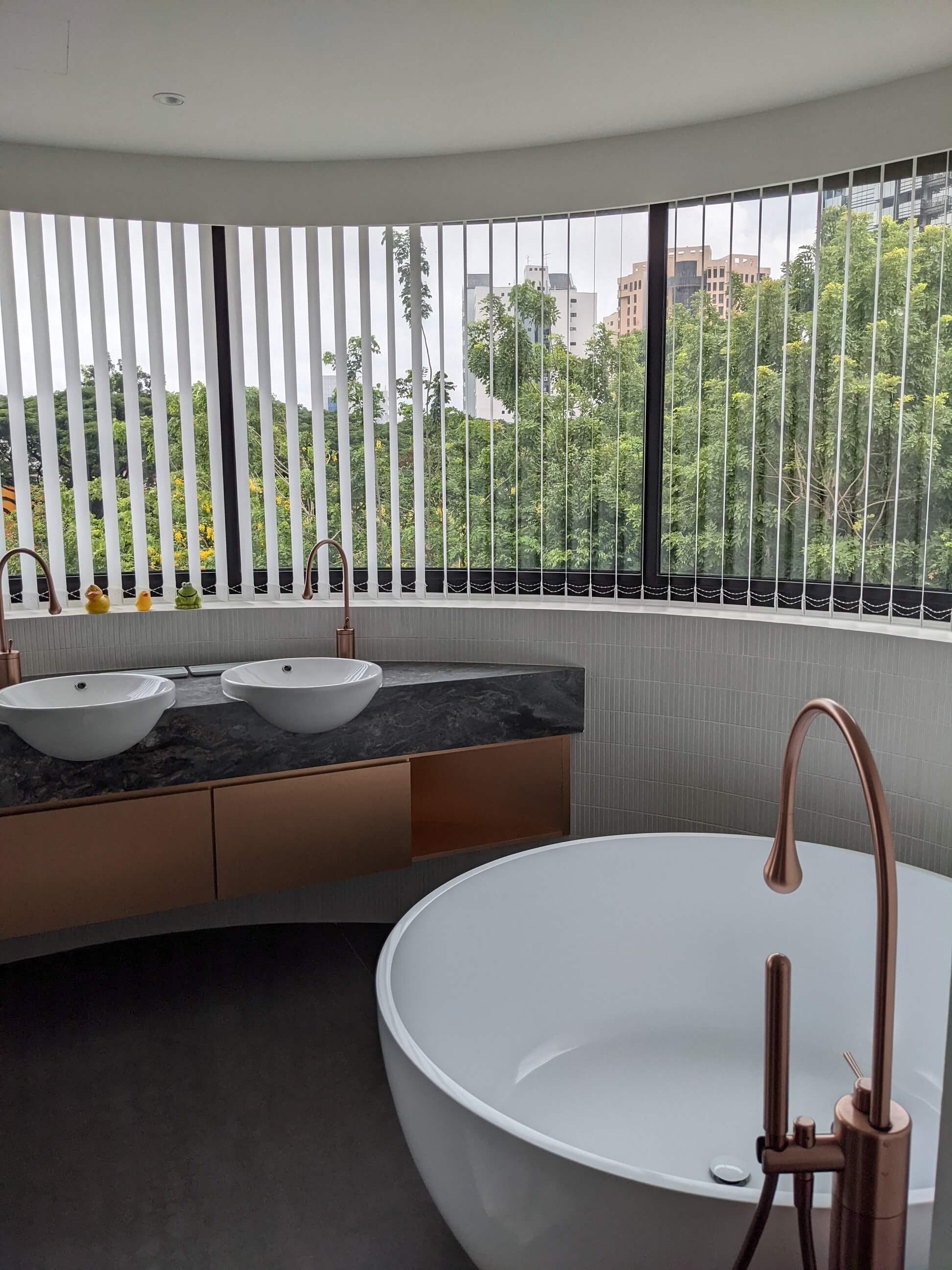 The girls' bathroom curved window frames the treetops, resplendent with a freestanding tub and copper-coloured fittings.