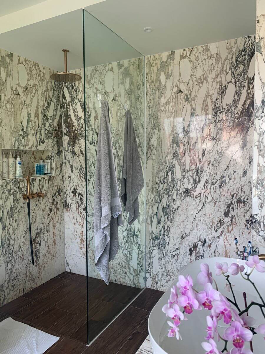 The master bathroom is a marble-clad walk-in shower with copper-coloured fittings and dark timber floor tiles.